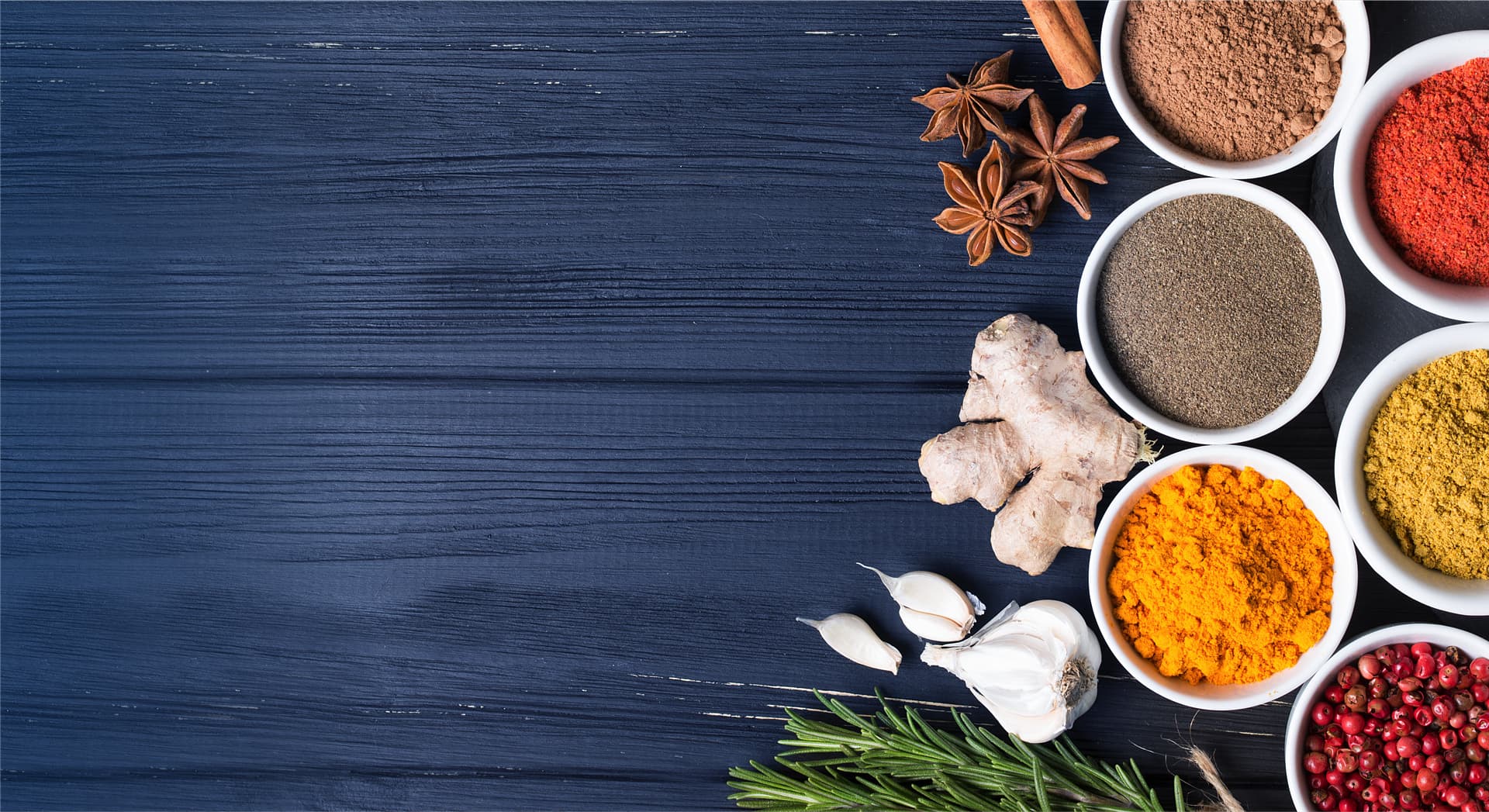 A photo of an assortment of freshly ground spices and fresh ginger root, star anise and garlic cloves.